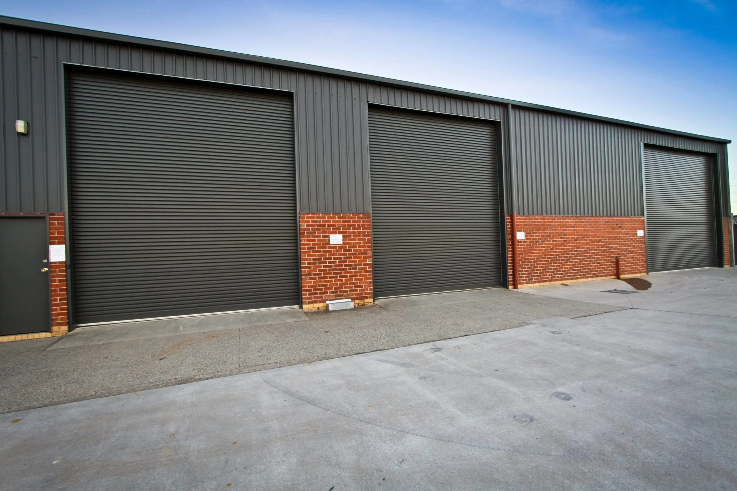 Three charcoal commercial roller shutter doors on a warehouse