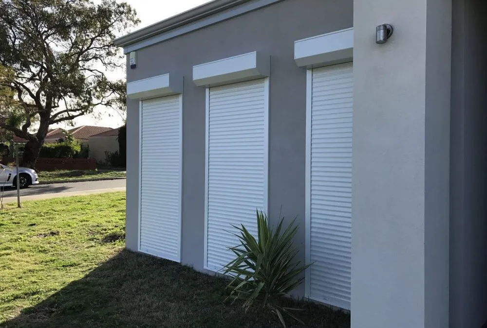 Two white roller shutters with pelmets on a dark grey rendered wall