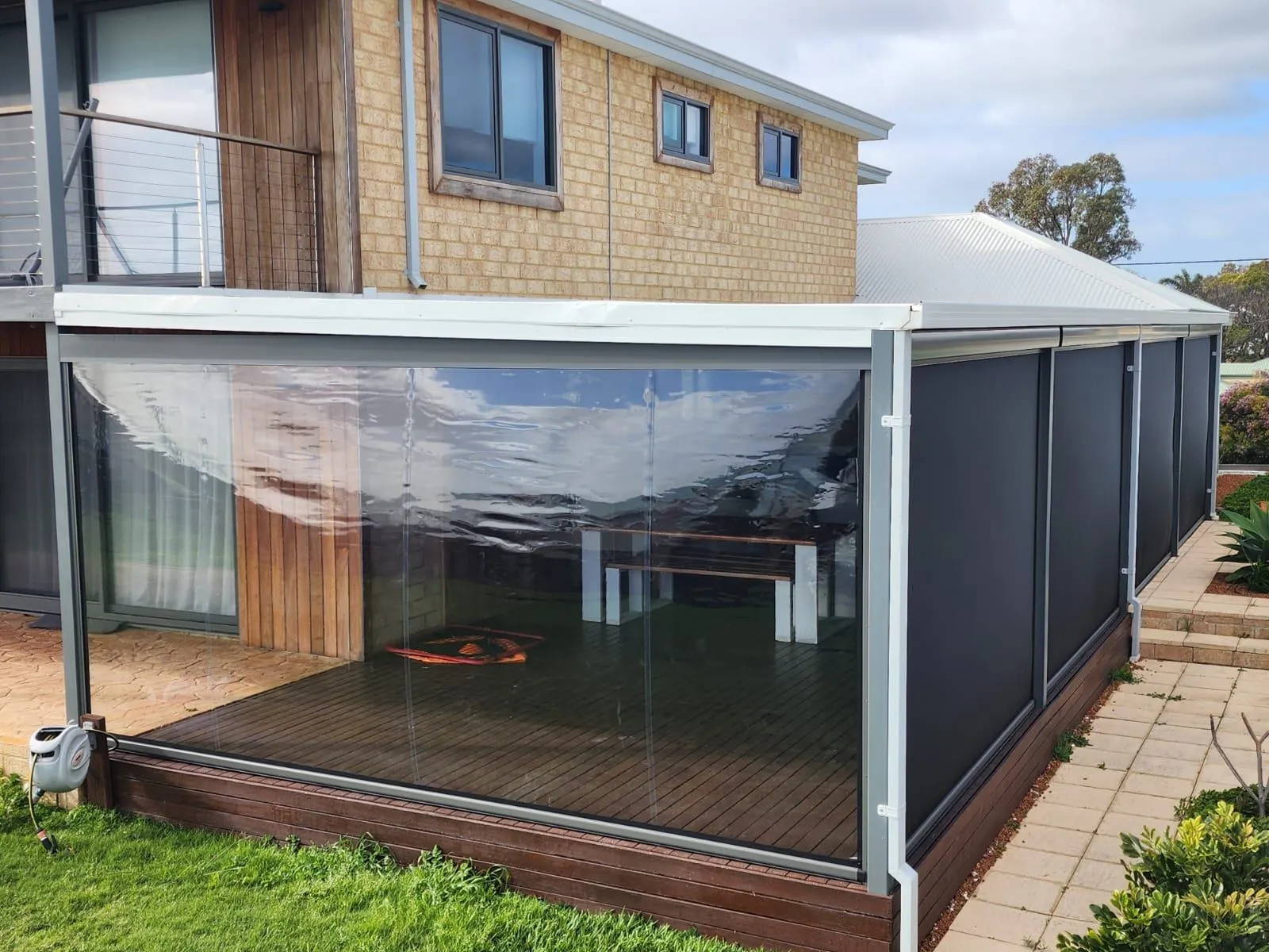 Outdoor blinds closing in a timber-decked patio on a two storey home