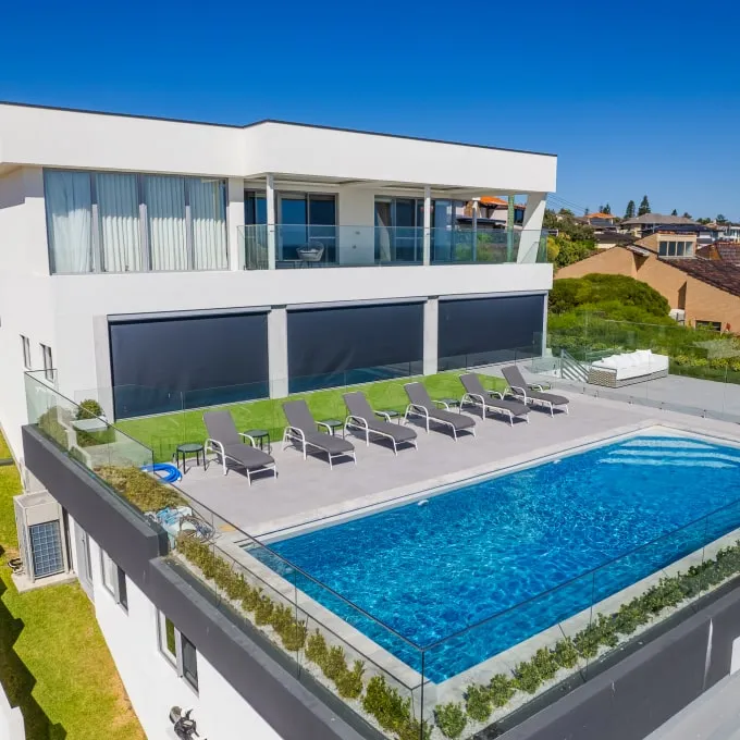 Outdoor blinds on the lower level of a modern home beside a pool