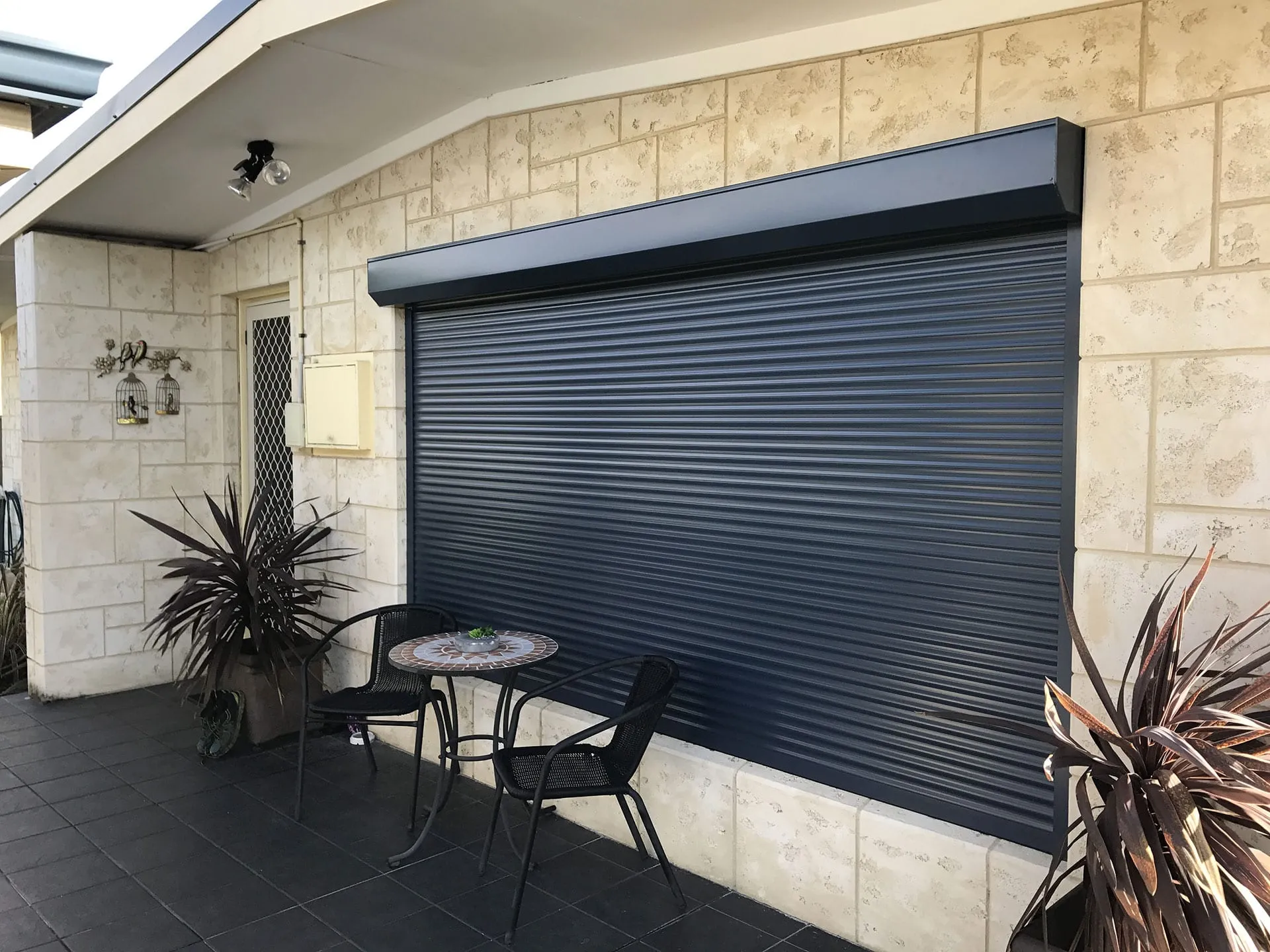 Dark grey roller shutter installed over a wide window on a limestone-block Perth home