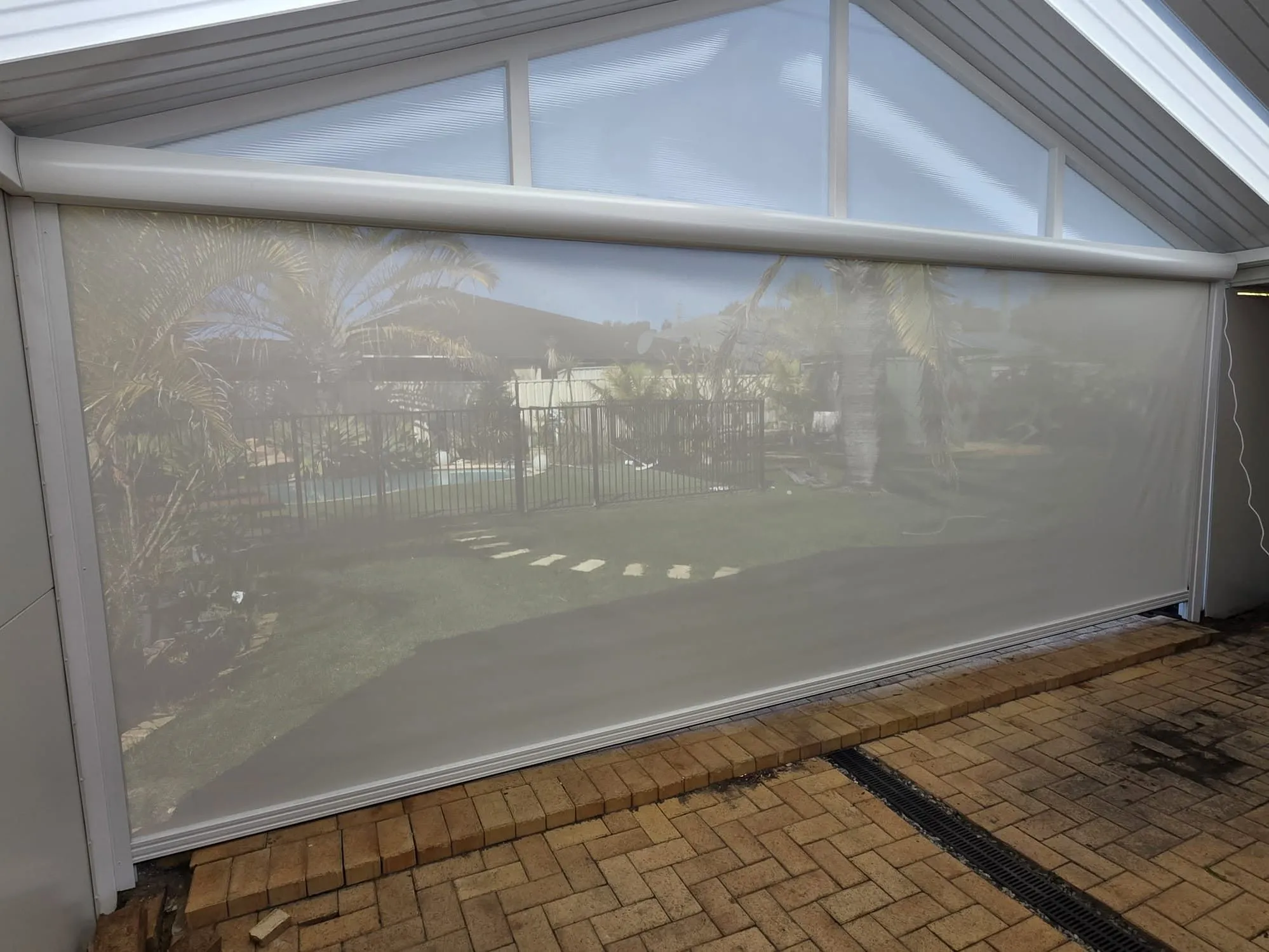 Cream Slidetrack blind lowered under a gabled patio roof, seen from inside