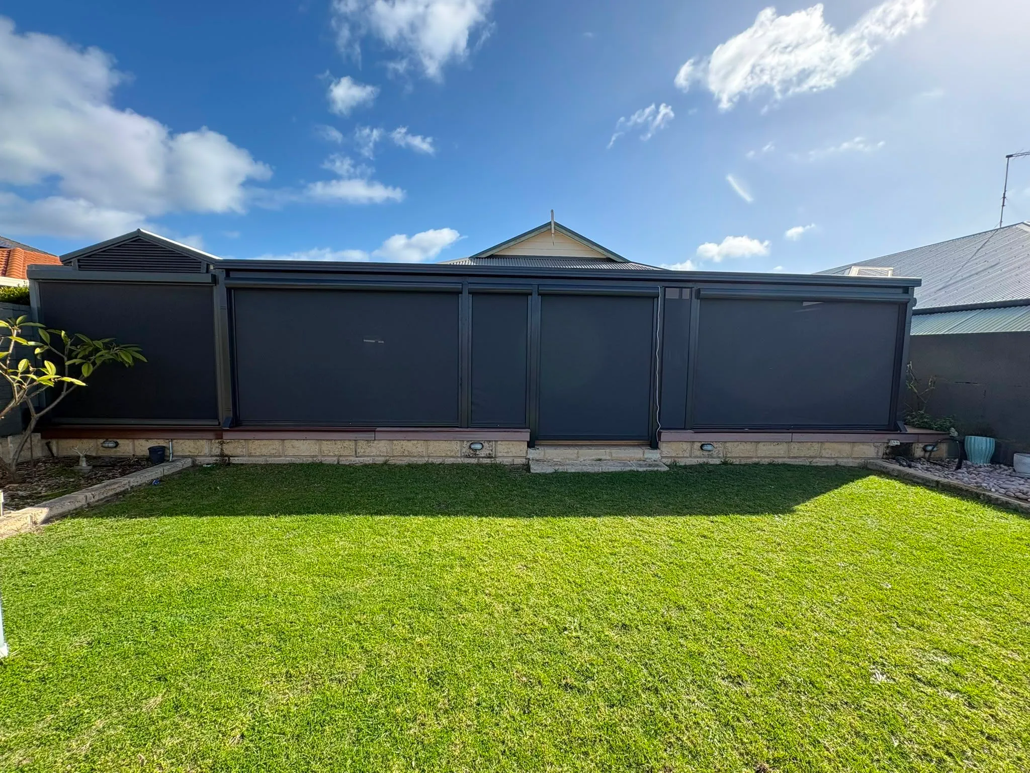Three charcoal Slidetrack blinds enclosing a patio on a Perth home, seen from the lawn