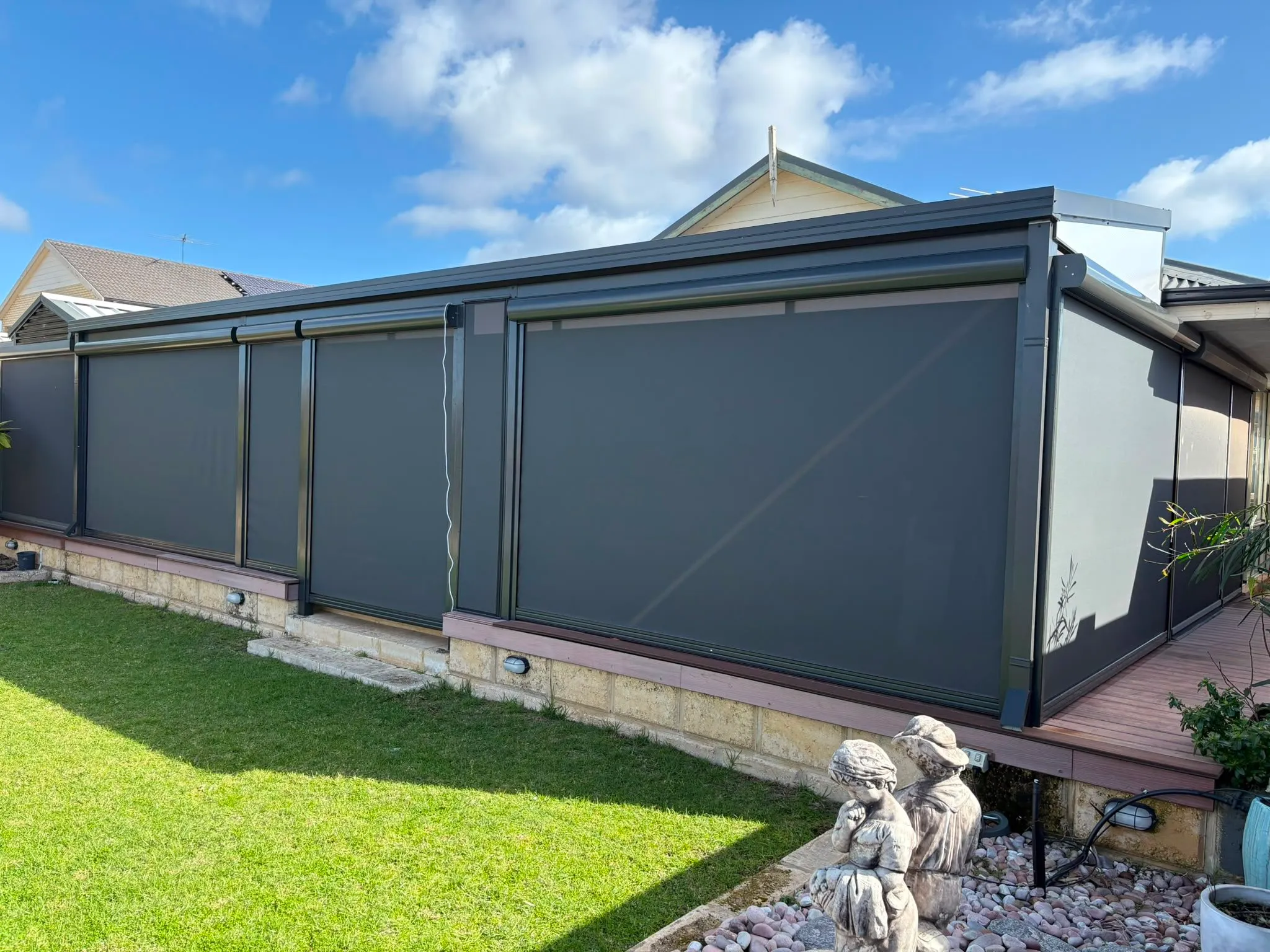 Three charcoal Slidetrack blinds along a patio with limestone edging and lawn
