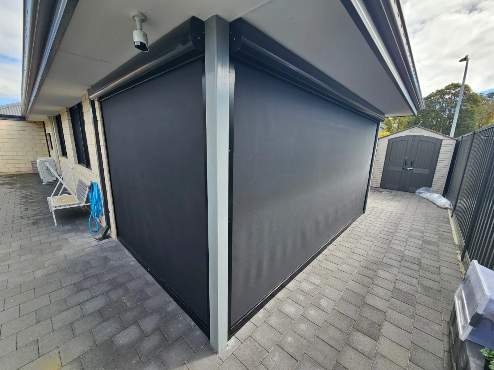 Charcoal Slidetrack blinds enclosing a paved alfresco, seen from the side path