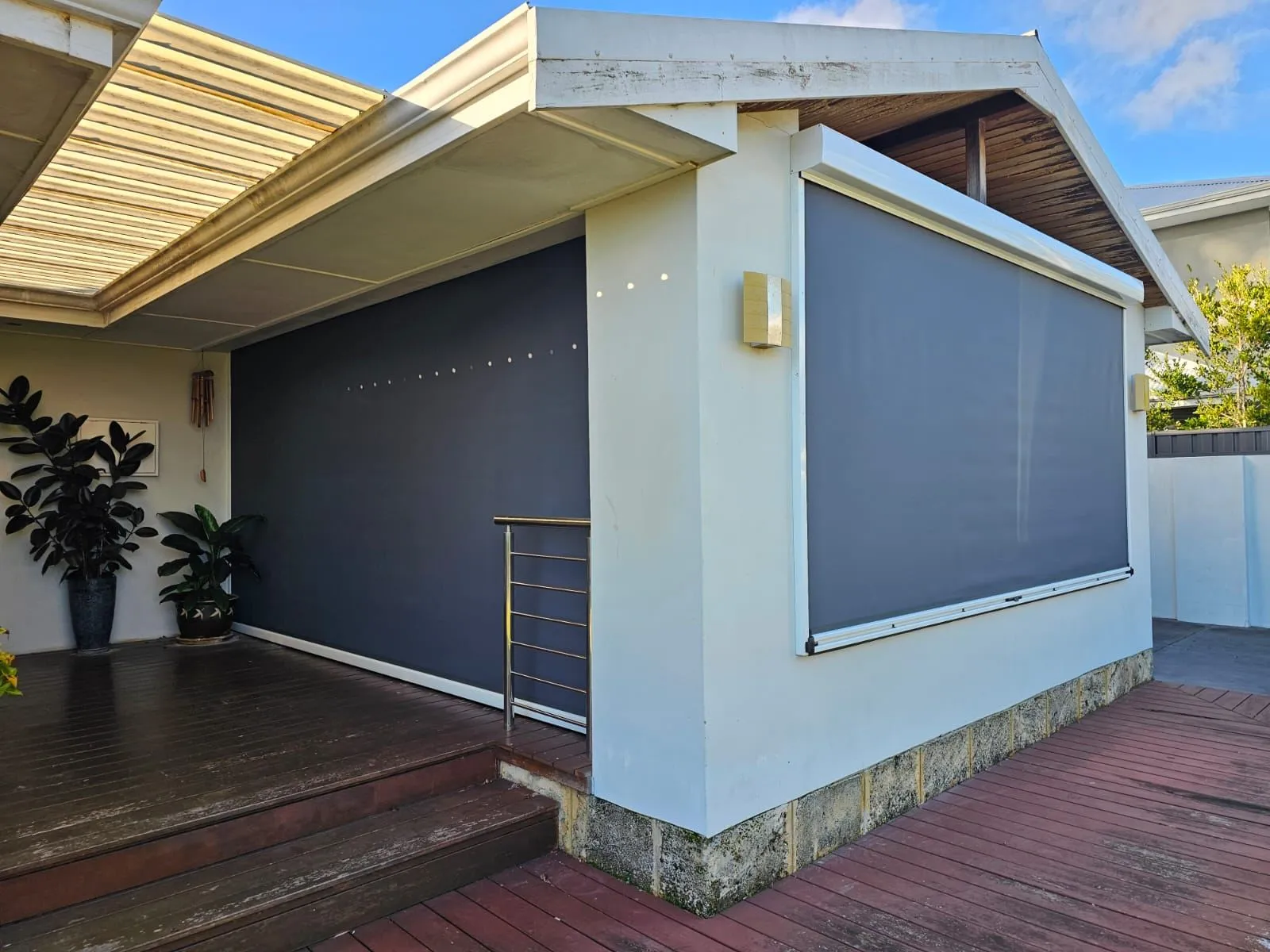 Charcoal Slidetrack blinds fully lowered on a rendered alfresco beside deck stairs