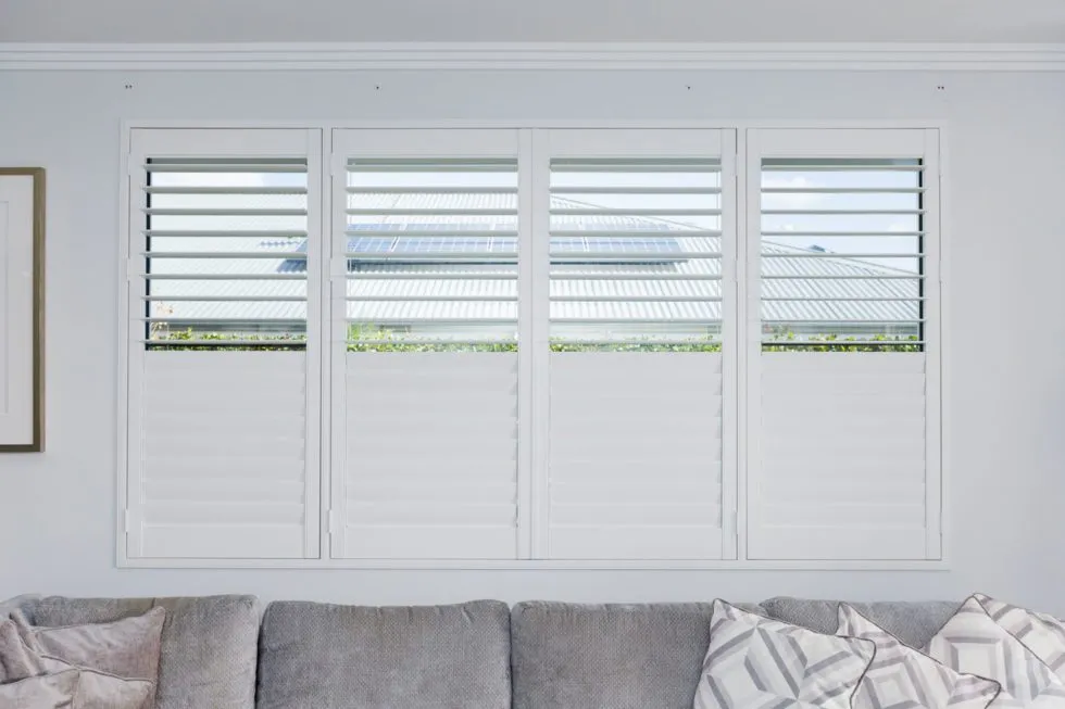 Four white plantation shutter panels with the upper louvres open above a grey sofa in a Perth home